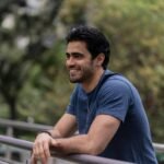 Smiling man leaning on railing outdoors in relaxed urban setting.