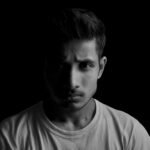 Dramatic black and white portrait of a young man with serious expression and dark background.