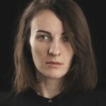 A striking portrait of a woman with short hair and a serious expression against a dark background.