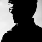 Artistic black and white profile silhouette of a man wearing eyeglasses.