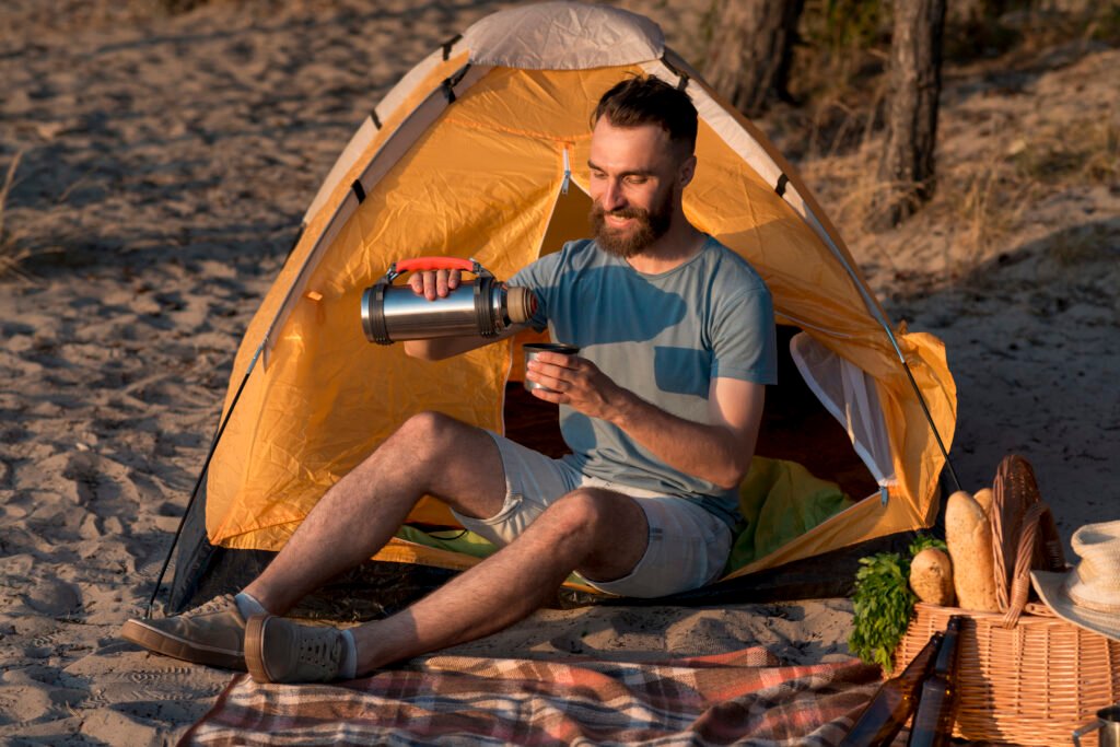 Camping tent pitched in a forest clearing with trees and mountains in the background.